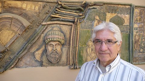 Mehmet Abu devant son cabinet et la fresque représentant Ibn Sina, plus connu sous le nom d'Avicenne.